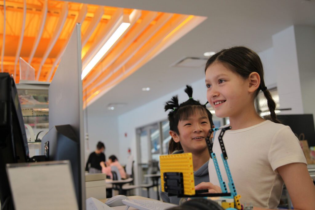 Two students smiling and showing their LEGO engineering project during a collaborative workshop at Valley Robotics Club in Fox Valley.