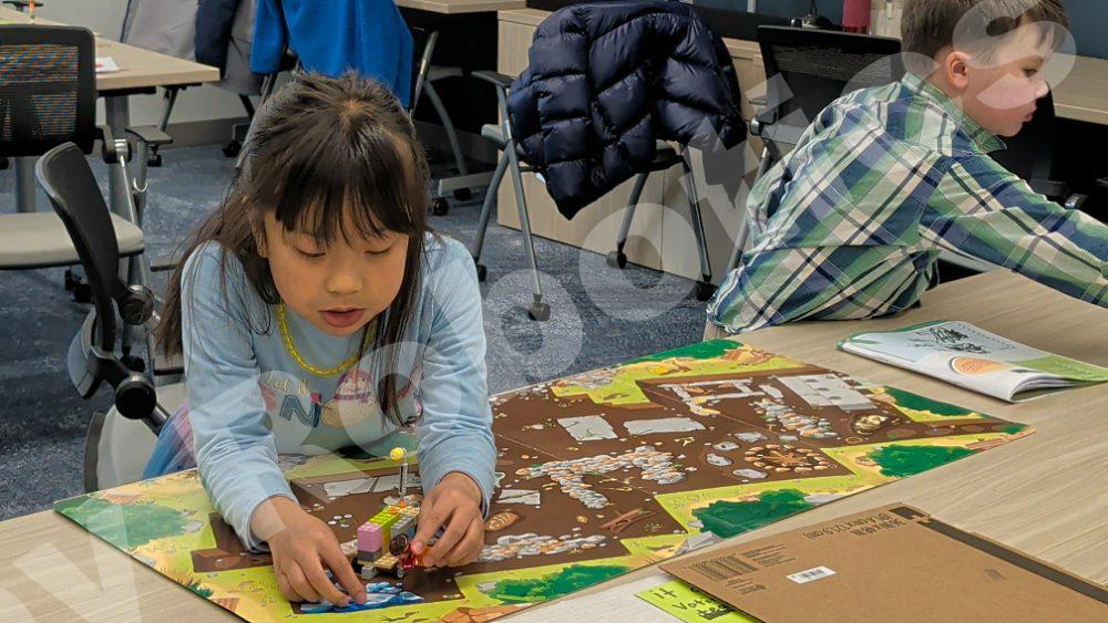 Two young students collaborating on a Lego robotics project over a colorful activity mat during a 2025 Fall Program class.