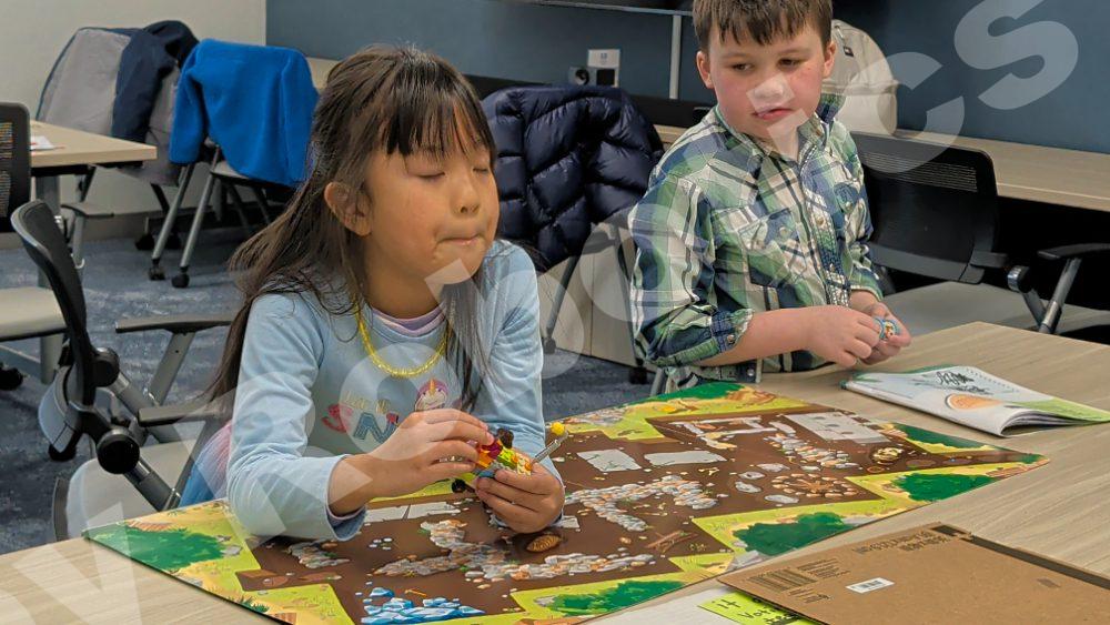 Two young students collaborating on a Lego robotics project over a colorful activity mat during a 2025 Fall Program class.